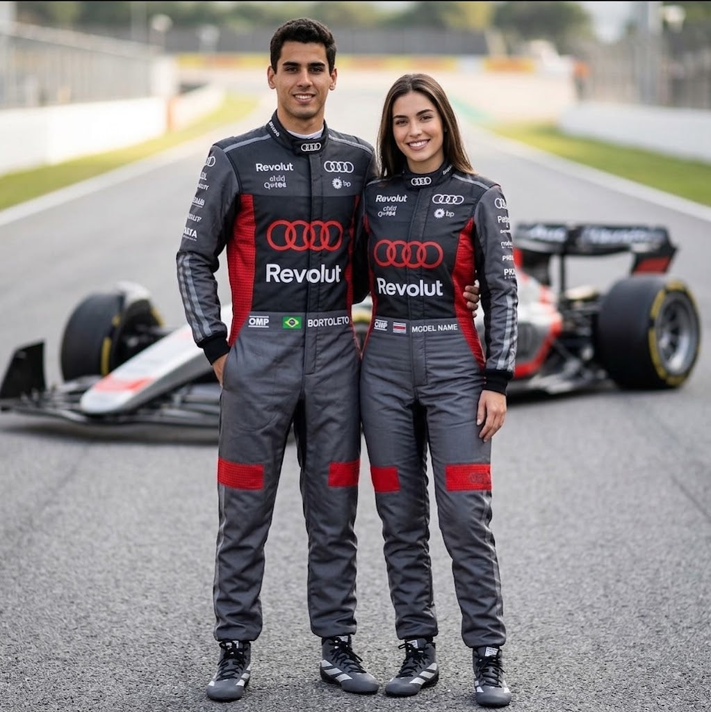 Man and woman in black and red Audi-style racing suits with an open-wheel car